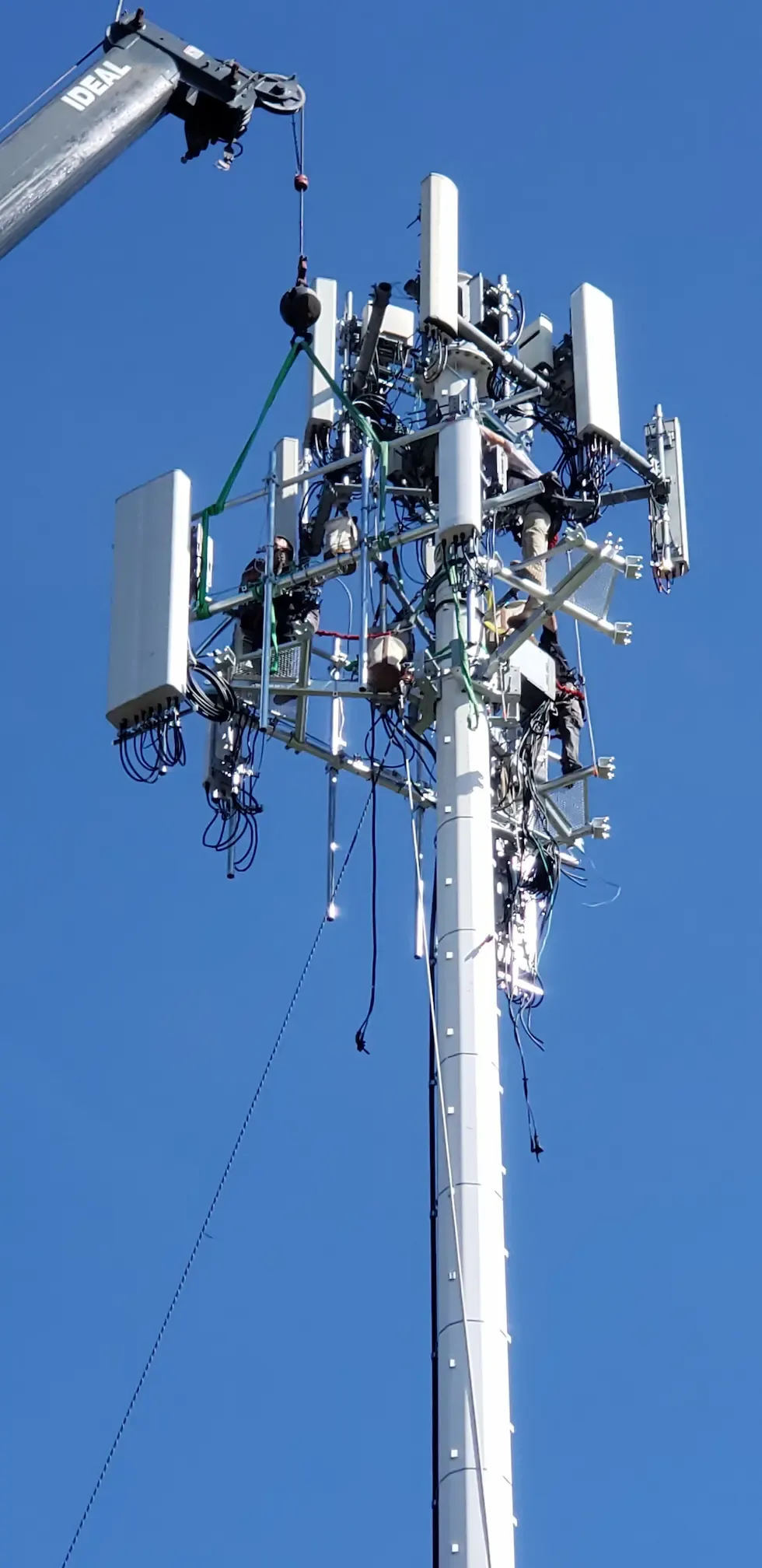 Crew installing antennas on a cell tower with crane support