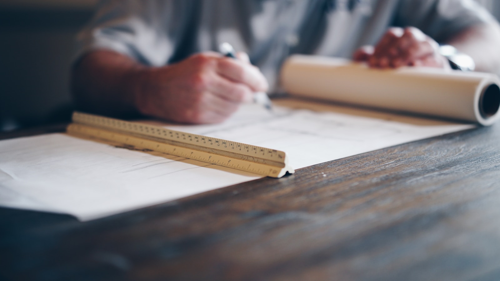 Engineer drafting site plans with a scale ruler and rolled drawings